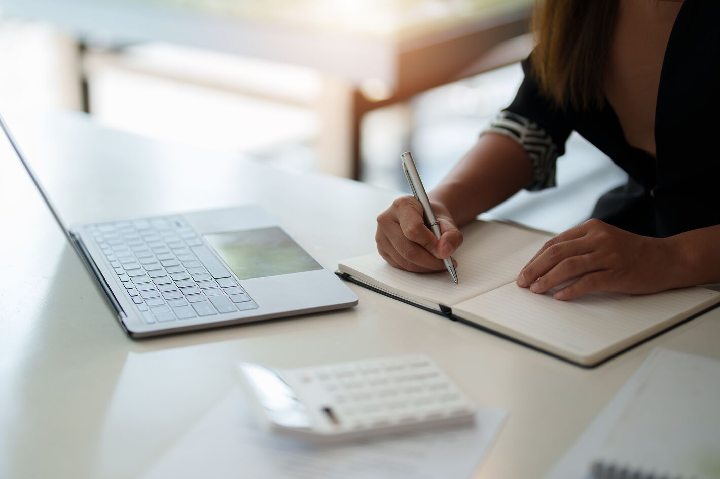 Zugeschnittenes Foto einer Frau, die sich Notizen beim Arbeiten oder Lernen am Laptop macht, Bild vermittelt eine online-Lehrgang oder online-Ausbildung bzw. ein online-Seminar-Situation.