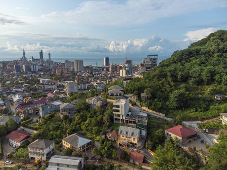 Cityscape with residential houses on a hillside and high-rise buildings in the background under a cloudy sky
