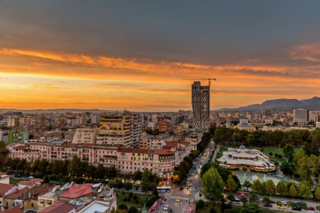Cityscape at sunset with a high-rise building and mountains in the background