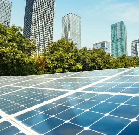 Solar panels on a rooftop with a row of skyscrapers and trees behind