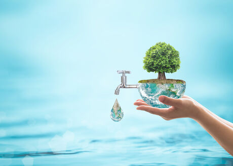Hand holding small green plant on palm with faucet dripping water