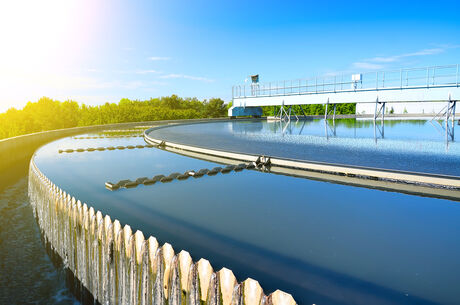 Circular water basin of a wastewater treatment plant with overflowing water and railing in the background