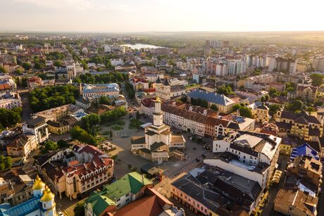 Aerial view of a city with a central square surrounded by historic and modern buildings at sunset.