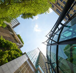 Upward view of modern high-rise buildings with glass facades and green walls under a blue sky with few clouds